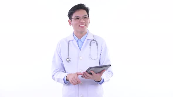 Happy Young Asian Man Doctor Thinking While Using Digital Tablet