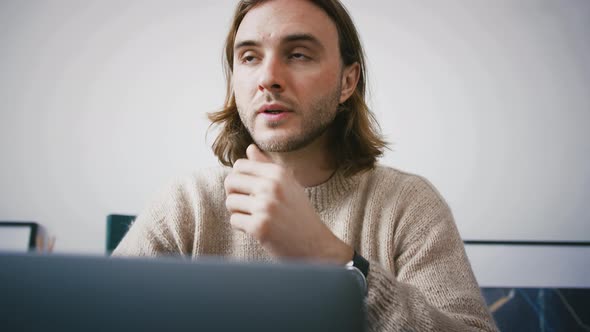 Young Handsome Male Entrepreneur in Casual Outfit is Looking Thoughtful While Working Sitting at a