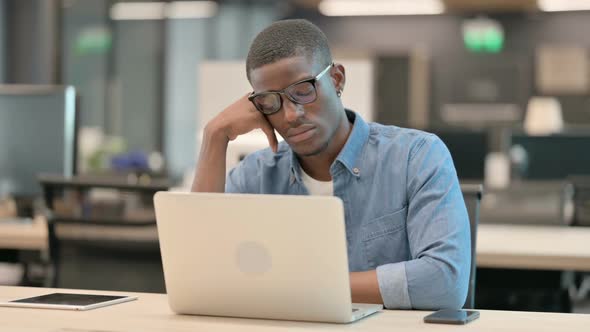 Young African American Man with Laptop Taking Nap in Office