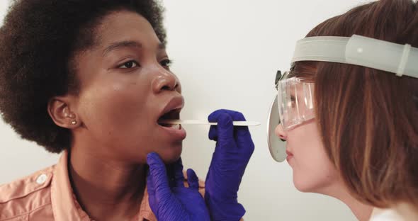 Otolaryngologist Examines A Female African American Throat With A Wooden Spatula