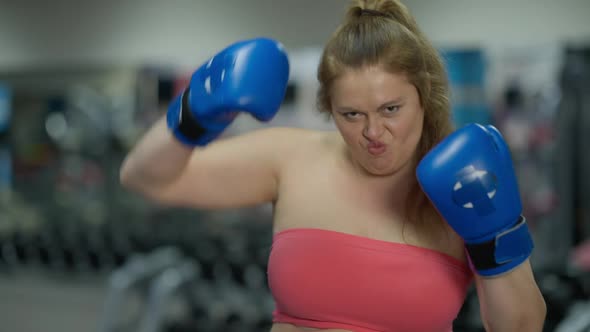 Positive Overweight Woman Grimacing Boxing Shadow Standing in Gym Indoors Looking at Camera