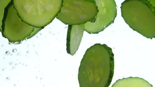 Cut slices of fresh cucumber in water over white background