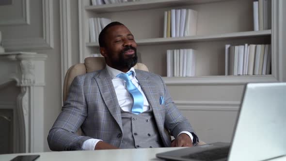 Funny African-American Bearded Man in a Gray Suit, White Shirt. The Businessman Is on the Desktop
