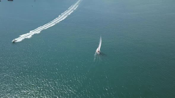 Flying over sail boat and speed boat. Sky view of boats on ocean in England.