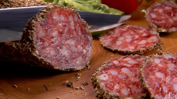 Dry Delicious Sausage in Herbs Is Sliced with a Knife on a Wooden Board