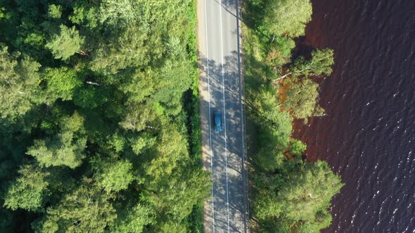 Asphalt Road with Driving Cars Through Green Summer Forest Near Lake. Aerial Shot From Drone