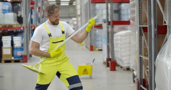 Funny Male Janitor Dancing with Mop in Warehouse