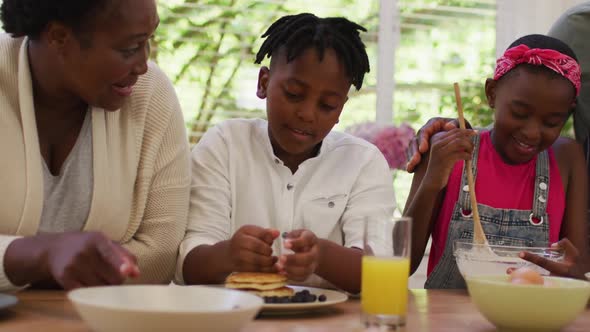 African american grandparents and grandchildren preparing pancakes in the kitchen at home