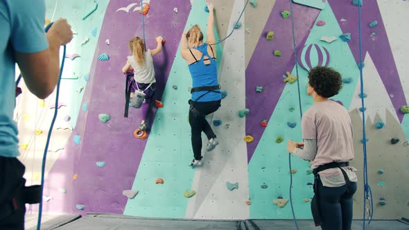 Group of People Climbing Up Artificial Wall and Belaying From the Ground Indoors