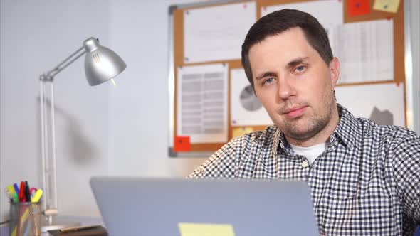 A Simple Man Looks at the Camera, in Front of Him Stands a Portable Laptop