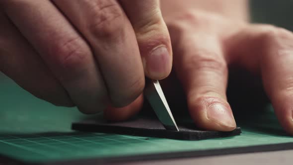 Man Hands Cutting Black Leather with Sharp Special Knife Closeup