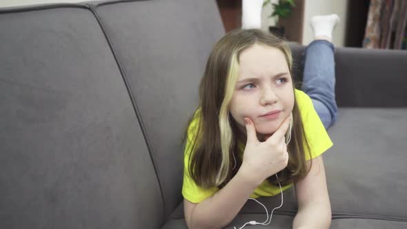 A Little Girl with Headphones Lying on the Couch