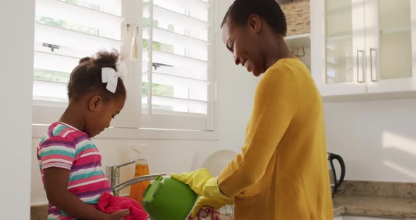 Happy african american mother and daughter washing dishes in kitchen