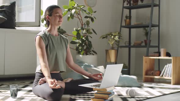 Woman Meditating in Lotus Pose with Online Yoga Class on Laptop