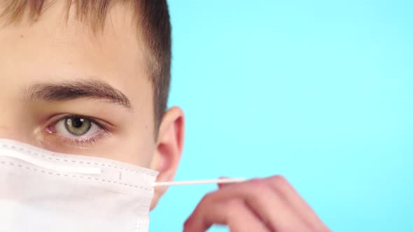 Young patient is putting on a medical mask on a bright blue background.