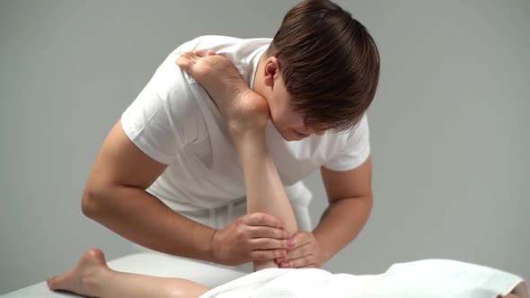 Male Masseur with Strong Hands Massaging Lower Part of Leg to Young Woman Lying on Massage Table