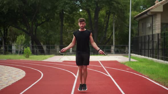 Fit Bearded Man Standing on Running Track Outdoors on Modern Stadium Doing Exercise with Skipping