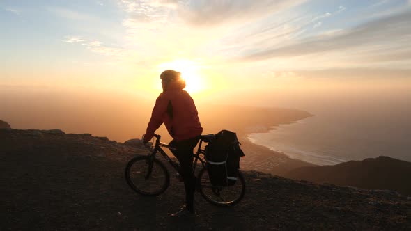 Man on a Bicycle High in Mountains Near Cliff Edge 