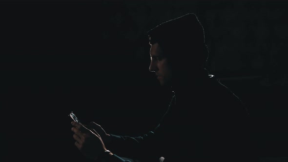 Silhouette of Man in Hood Scrolling News Feed on Smartphone.