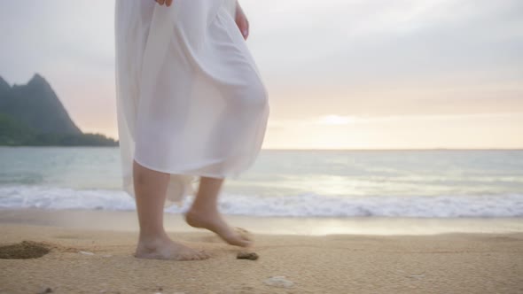 Slow Motion Woman in White Boho Dress Walking Barefoot By Beach at Golden Sunset