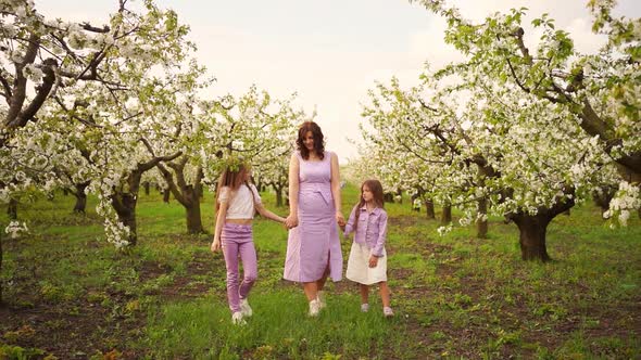 Mom Walks with Her Two Daughters in the Garden Among the Flowering Trees