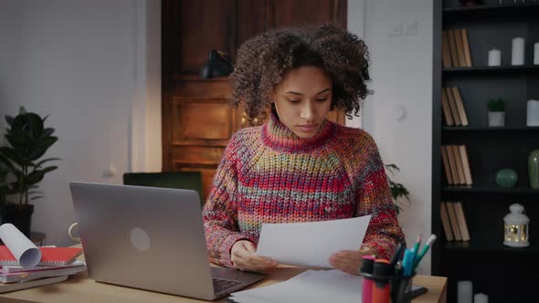 Young Curly African American Lady Freelancer Reading Documents and Working on Laptop From Home