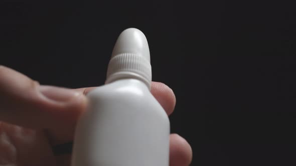 Close-up of a White Bottle in a Person's Hand on a Dark Background