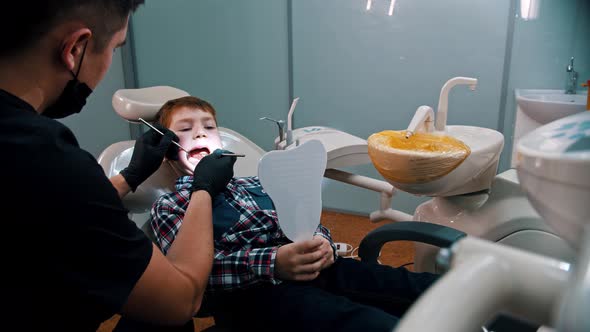 A Little Boy Having a Treatment in the Dentistry - the Boy Holding a Mirror and Looking at the