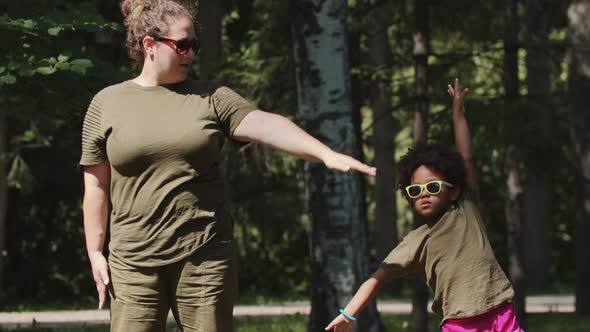 White Woman and Her Black Little Daughter Doing Simple Exercises in the Park