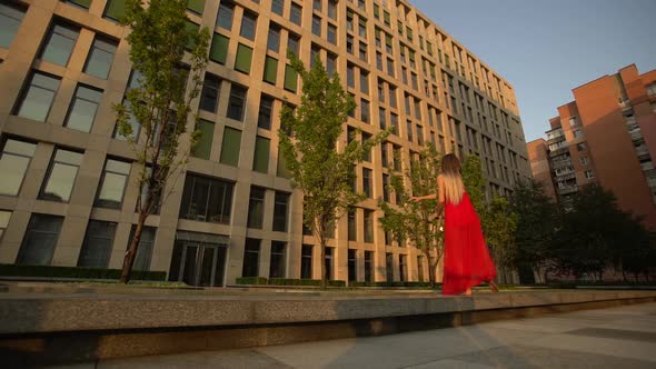 Beautiful Young Girl Dancing on the Street of a Modern Building of a Business Center in the Sunset