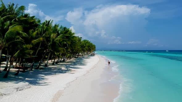 aerial of girl walking along beautiful white beach lined with palm trees. White beach, Panglao islan