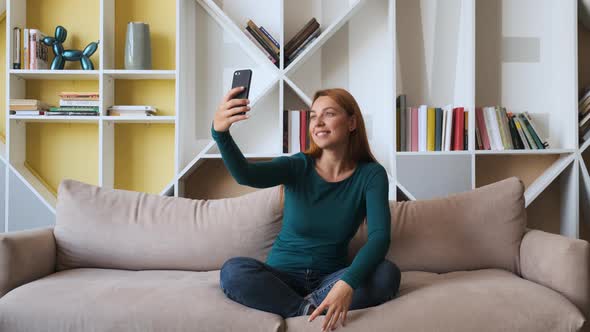 Young Attractive Woman Taking Picture with Her Smartphone Sitting on Sofa at Home.
