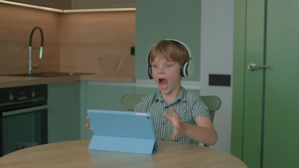 Upset Child Loosing Mobile Game Using Tablet Computer Sitting in the Kitchen