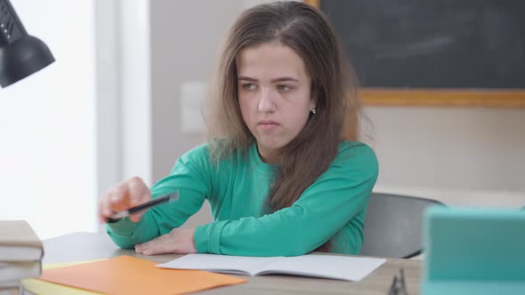 Concentrated Caucasian Woman Writing with Pen Sitting at Desk Sighing Tired with Studies