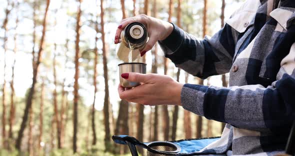 Young female tourist pouring hot beverage from thermos into cup