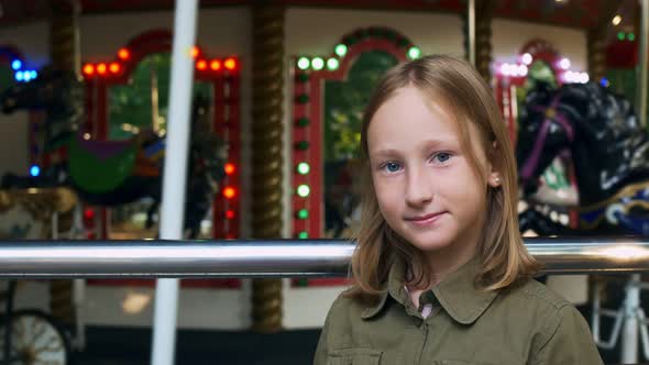 A Portrait of a Teenage Girl Blonde with Blue Eyes Stands Happy in an Amusement Park at a City Fair