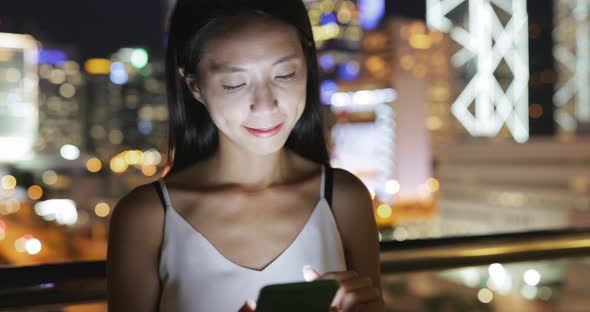 Woman looking at mobile phone with the background of cityscape in Hong Kong 