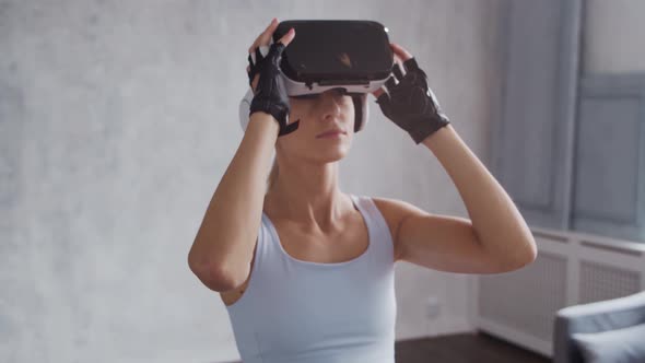 Young and sporty girl in sportswear is doing exercises at home using virtual reality helmet.