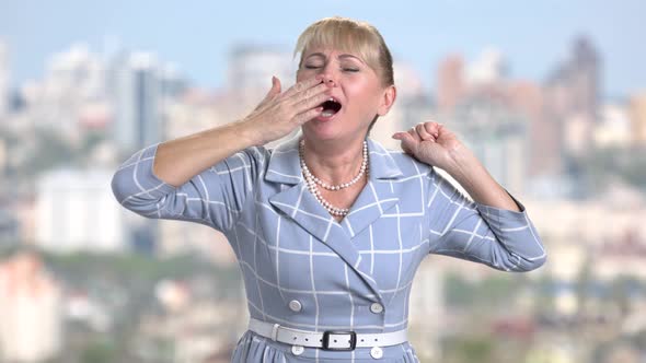 Middle-aged Woman Is Yawning on Blurred Background