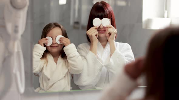 Woman Standing in Front of Her Daughter in the Bathroom and Cleaning Her Face with a Cotton Pad