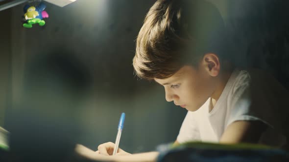 Young Male Child is Very Concentrated Doing His Homework at Desk in His Room