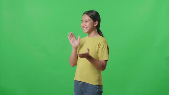 Side View Of Young Asian Kid Girl Clapping Her Hands In The Green Screen Studio