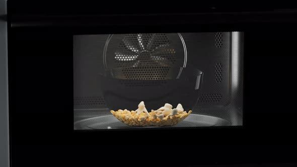 Popcorn preparation. Corn seeds popping up from glass bowl at the microwave.