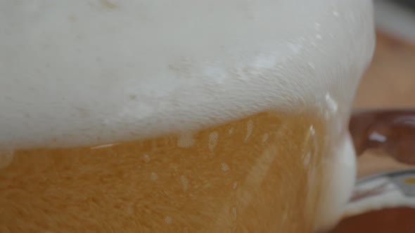 The tip of a crystal beer glass in focus as the beer is being poured, and the frothy foam fills the