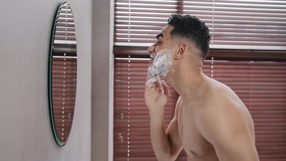 Side View Cheerful Happy Naked Arab Indian Man in Shower Looking in Mirror Smearing White Foam Face