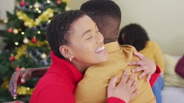 Happy diverse male and female friend hugging in front of christmas tree at home