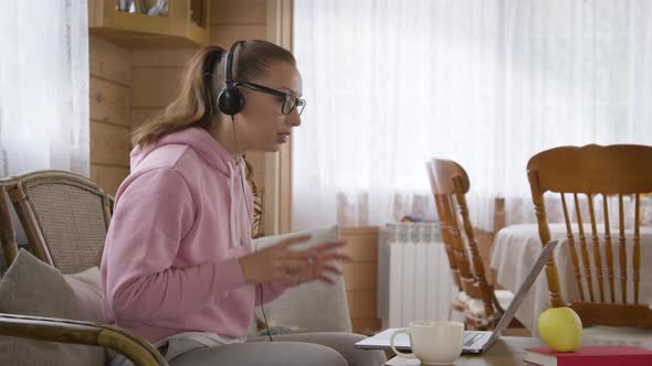 Woman in a Hoodie Communicates with Colleagues From Home Using a Laptop.