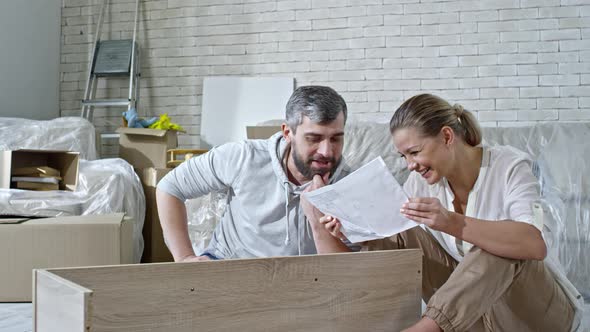 Laughing Couple Inspecting Assembling Manual for Shelf