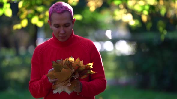 Young Homosexual Man with Pink Hair Is Walking in Autumn Park at Sunny Weather, Holding Bouquet From