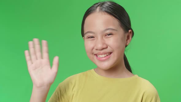 Happy Asian Kid Girl Waving Hand And Say Bye Bye While Standing On Green Screen In The Studio
